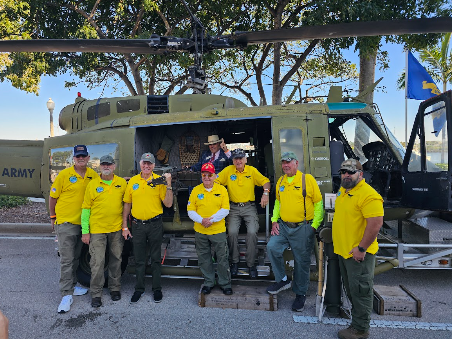 A group of men in yellow shirts standing in front of a military vehicle.
