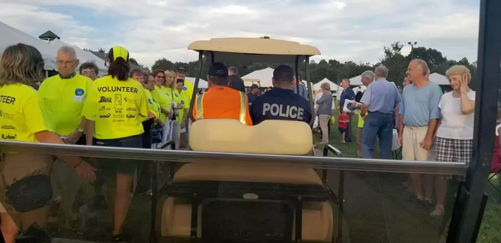 A group of people in yellow shirts standing around a police vehicle.