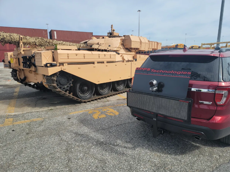 A red car parked next to a large tank.